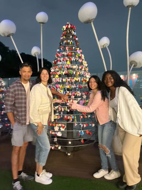 Evening photo of four travelers posing by a colourful padlock tree; image slightly soft in focus.