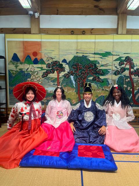 Travelers dressed in traditional hanbok pose in front of a colourful Korean painted screen with deer and pines.