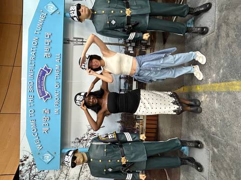 Two visitors wearing helmets pose beneath a sign for the 3rd Infiltration Tunnel at the DMZ.