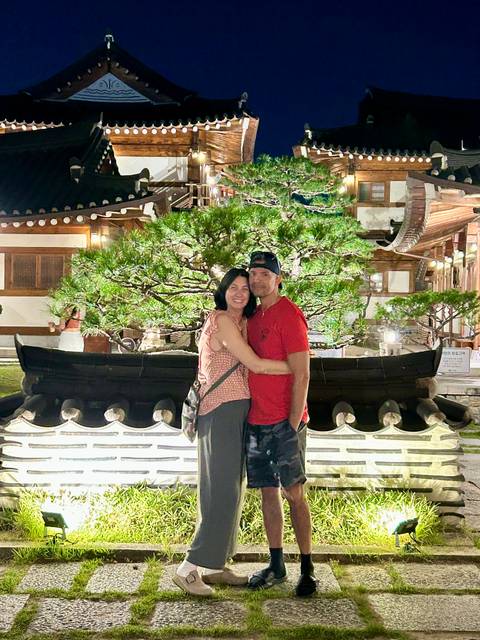 Couple embracing beside a beautifully lit bonsai pine in a traditional courtyard at night.