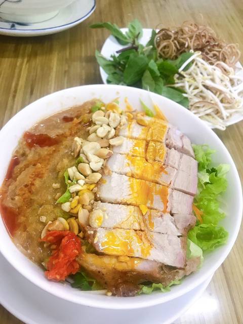 Bowl of Vietnamese noodles topped with roast pork slices, crushed peanuts and rich orange sauce.
