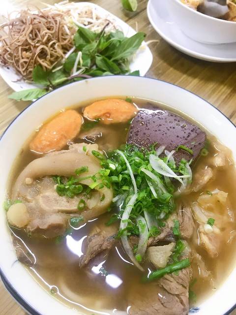 Steaming bowl of Vietnamese beef noodle soup with pork hock, blood cube and bright green scallions.