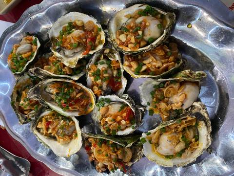 Tray of grilled oysters generously topped with peanuts, herbs and chili sauce.