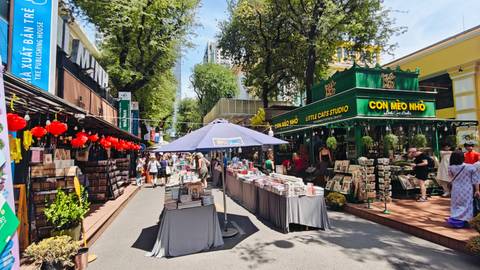 Outdoor pedestrian book street with stalls of books and shaded seating under tall trees in Ho Chi Minh City.