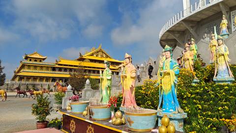 Golden pagoda complex with colorful Buddhist statues and ornamental gardens under blue sky.
