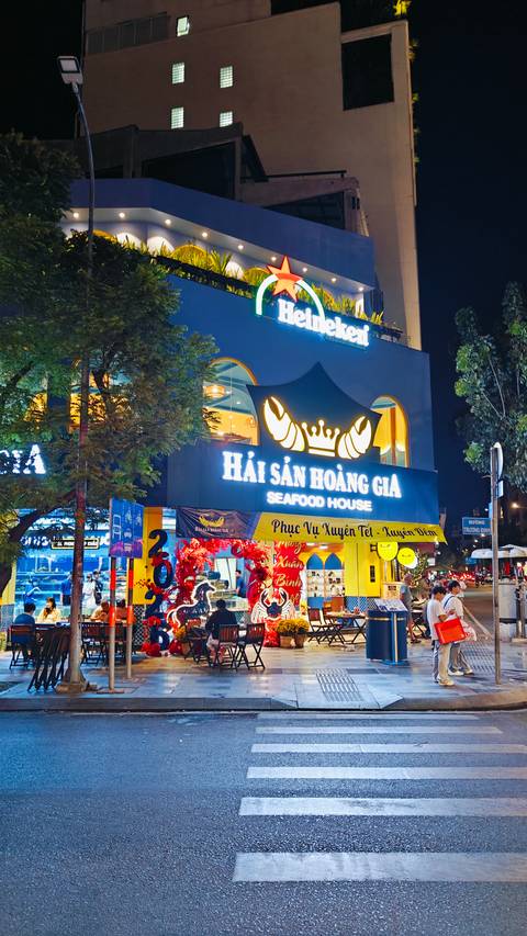 Brightly lit seafood restaurant storefront at night with large crab logo and Vietnamese signage.