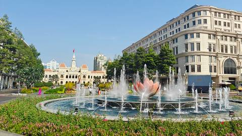 Fountain with pink lotus sculpture on Nguyen Hue pedestrian street facing Ho Chi Minh City Hall and colonial buildings.