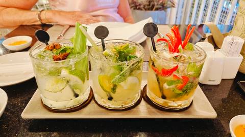 Trio of vibrant cocktails garnished with herbs, star anise and chili peppers on a restaurant table.