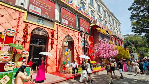 Colorful storefronts with lanterns, flowers and crowds celebrating outside a decorated building.