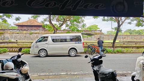 White minivan with bicycles parked outside a café, historic Vietnamese wall in background.