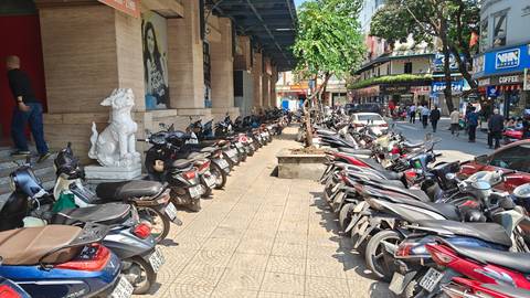 Long row of parked motorbikes lining a busy urban sidewalk in Vietnam.