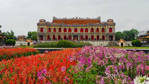 Ornate Imperial City palace in Hue framed by vibrant red and purple flower beds.