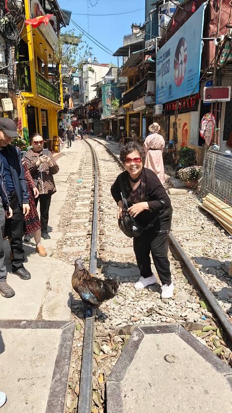 Tourists posing on the narrow railway tracks of Hanoi Train Street in bright sunlight.