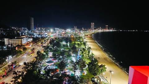 Nighttime aerial view of a brightly lit coastal city and long curved beachfront promenade.