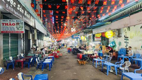 Night market street lined with plastic tables and red lantern bunting, bustling with diners and vendors.