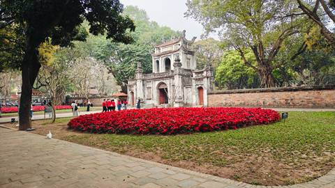 Historic stone gate of the Temple of Literature framed by red flower bed and mature trees.