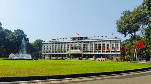 Reunification Palace with fountain and manicured lawn under clear blue sky and national flags.