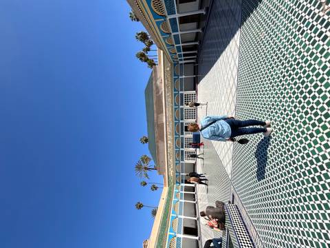 Visitors walk across the patterned courtyard of Bahia Palace in Marrakesh under a deep blue sky.