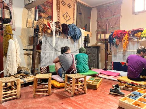 Artisans weave colourful carpets on looms in a traditional Moroccan workshop filled with dyed yarn.
