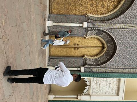 Close-up of tourists examining one of the ornate golden palace doors with intricate tile borders in Fes.