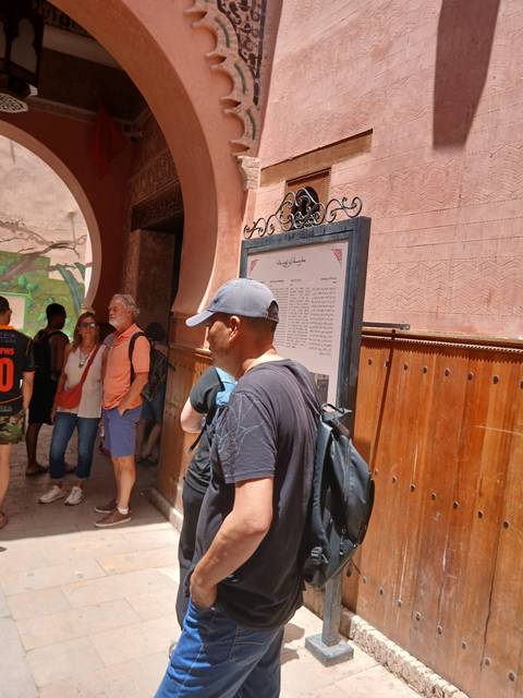 Tourists waiting near an entrance with Arabic information board in Marrakech.
