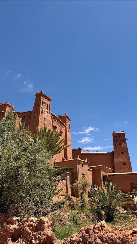 Red clay kasbah towers of Ait Benhaddou against clear blue sky.