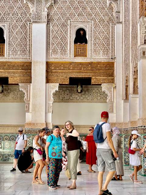 Tour group gathered in ornate courtyard with carved arches and mosaic tiles inside a historic Moroccan monument