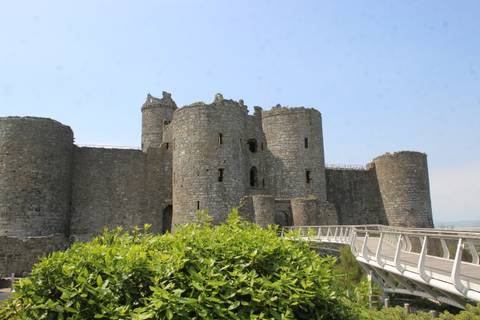 Medieval stone Pembroke Castle with round towers rising above greenery and modern walkway.
