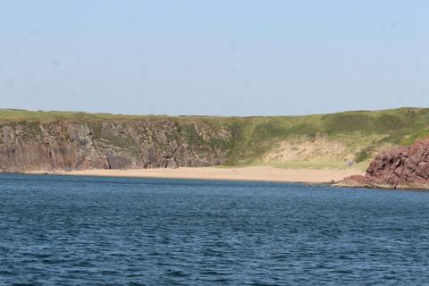 Remote sandy cove bordered by rugged green cliffs beside open blue sea.