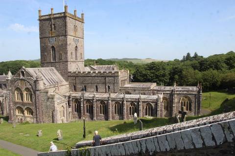 Stone Gothic cathedral with tall square bell tower set amid green countryside under blue sky