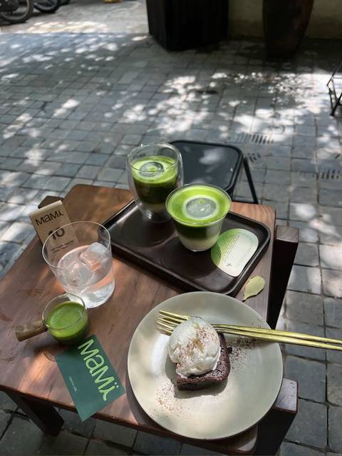 Outdoor café table with layered iced matcha drinks, glass of water and dappled shade on stone pavement
