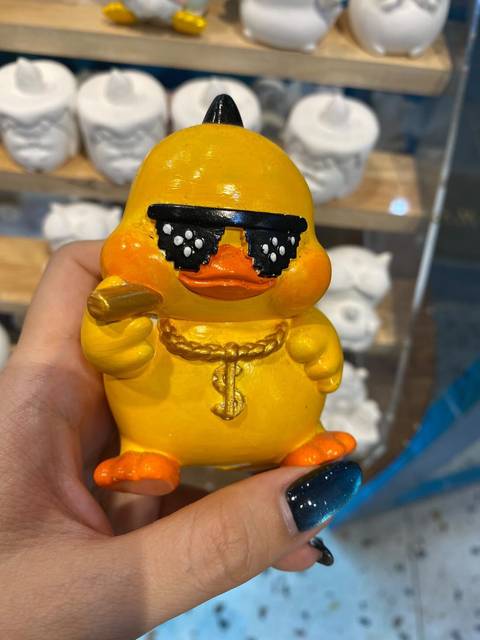 Hand holding a quirky yellow duck figurine with sunglasses and gold chain