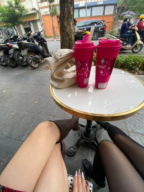 Small round café table on sidewalk with two takeaway drinks and shopper’s legs visible