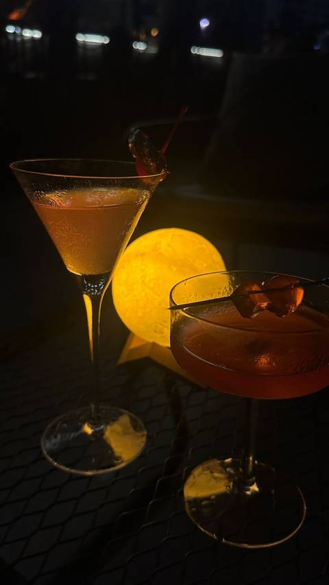 Two elegant cocktails beside a glowing moon-shaped lamp in a dimly lit setting