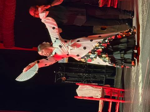 Flamenco dancer in polka-dot dress striking a pose on stage with raised fan