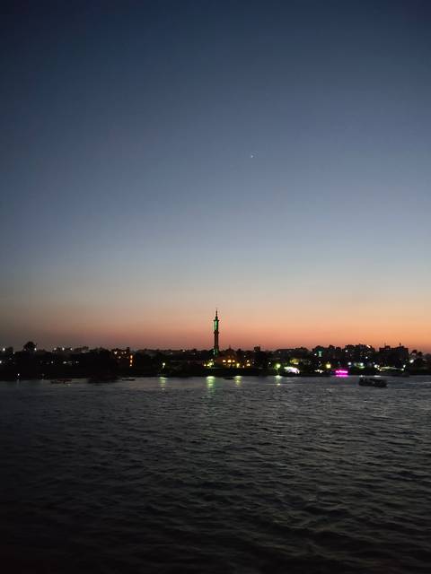 Sunset over the Nile River with city skyline and single illuminated minaret silhouetted against colorful sky