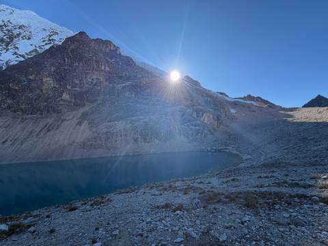 Early morning sun peeks over high Andean ridge illuminating a glacial lake below