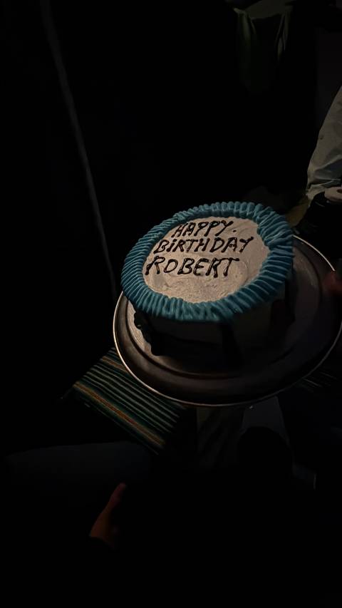 Dimly lit birthday cake with blue icing border and chocolate lettering