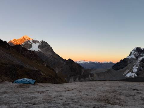 Snowy summit glows orange at sunrise above tent pitched on high mountain pass