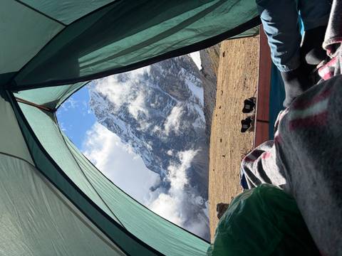 View from inside tent of towering snow-covered peak framed by shelter flaps and scattered clouds