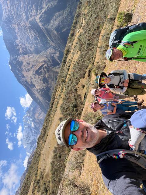 Smiling trekking party takes selfie on dirt trail with snowy Andes rising behind