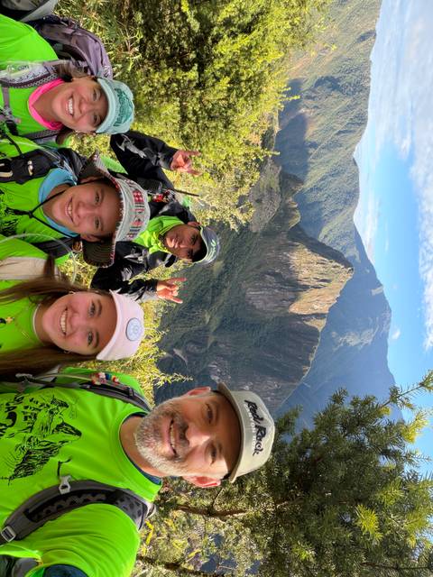 Happy trekkers in bright green shirts pose with Huayna Picchu towering behind lush forest