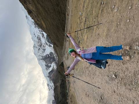 Cheerful hiker raises trekking poles triumphantly on snowy valley trail beneath glacier
