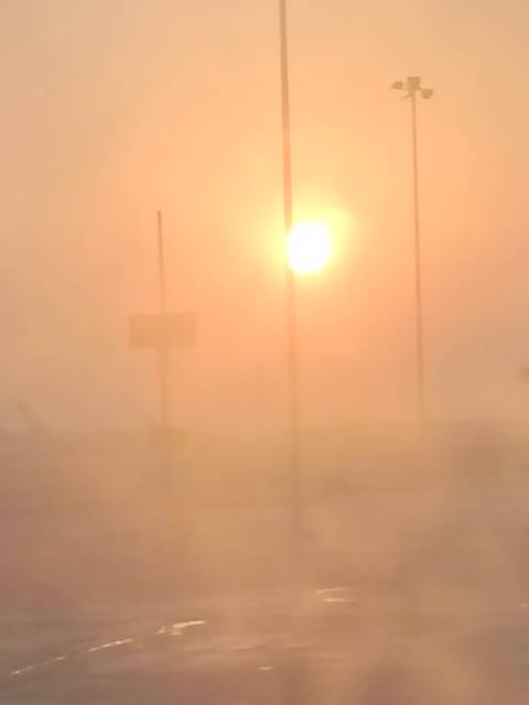 Hazy orange sun shining through thick dust or fog with faint silhouettes of poles