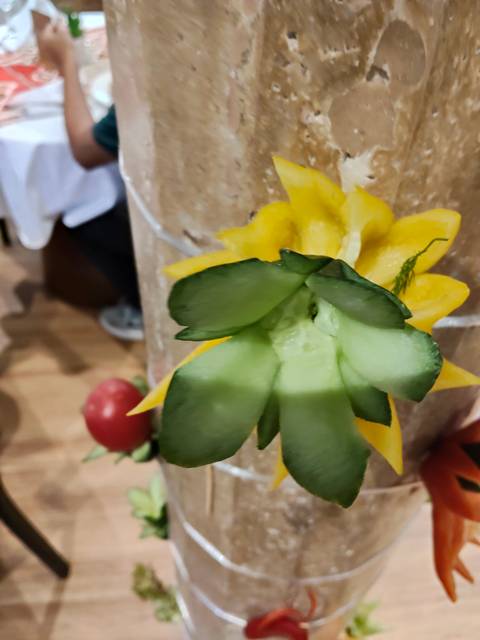 Close-up of a carved vegetable flower centerpiece in a dining setting, slightly out of focus