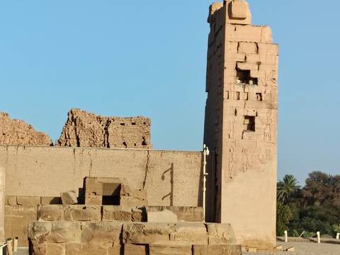 Ancient stone walls and a slender obelisk against a clear blue sky at an Egyptian temple