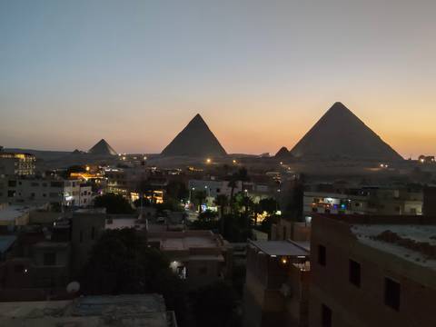 Evening panorama of the Pyramids of Giza rising beyond the city’s low rooftops at dusk