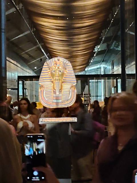 Soft-focus museum scene featuring Tutankhamun’s golden mask behind reflective glass