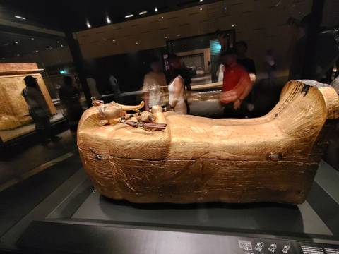 Golden sarcophagus displayed in a dark museum gallery with blurred visitors around