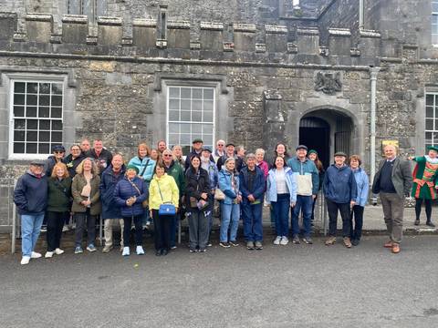 Large tour group posing happily in front of an old stone building with arched doorway